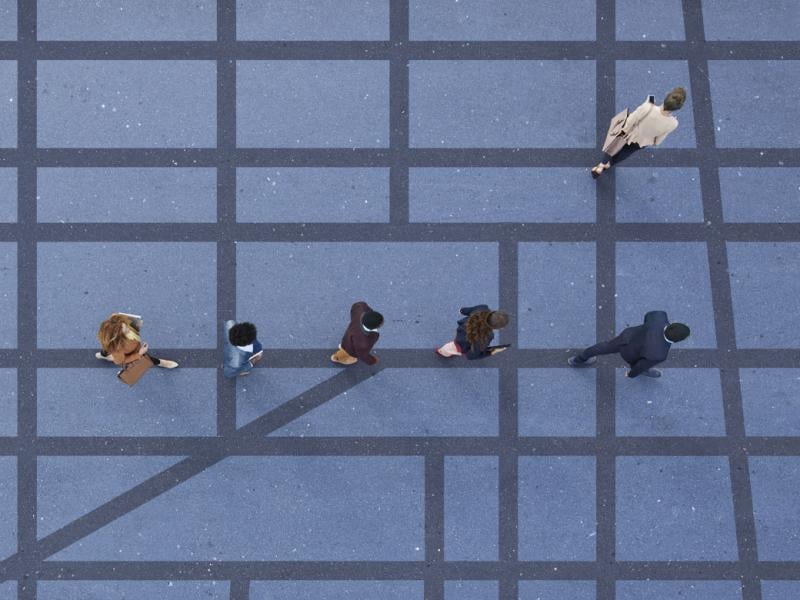 Seen from above, a single-file line of five people walking along a grid of dark grey lines against a lighter grey, with one lone woman standing apart from the group.