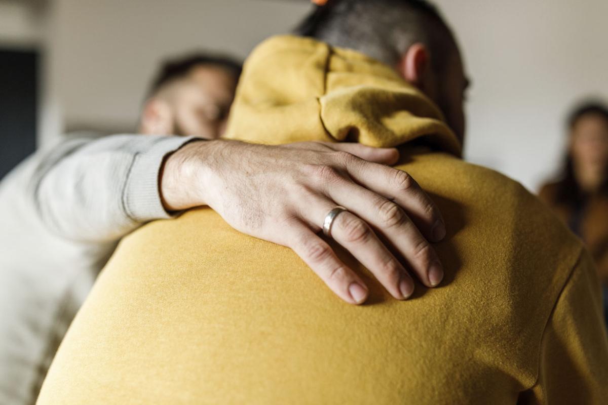 Person's hand embraces another's shoulders during a group discussion
