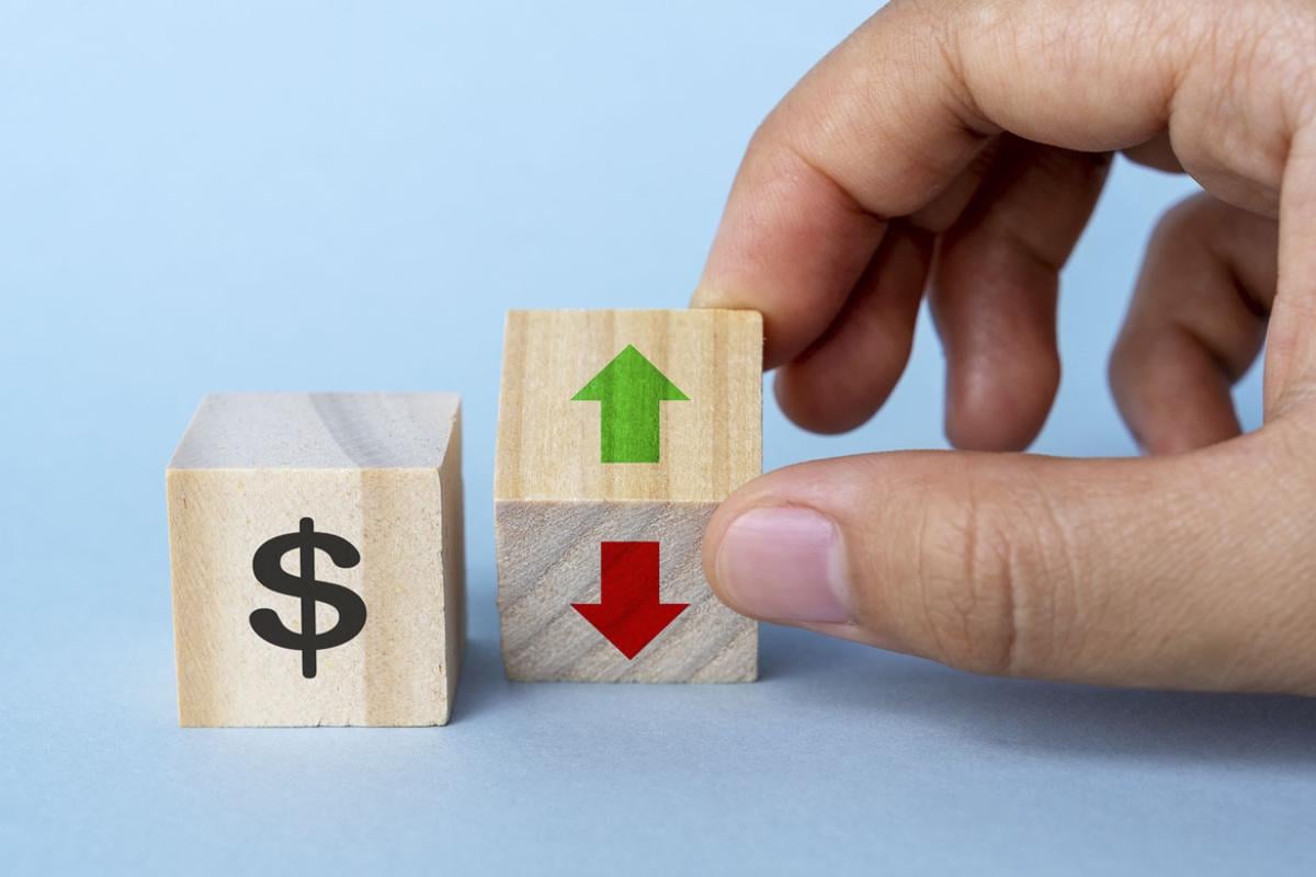 Hand holding a block with arrows, another block with a dollar sign sits nearby
