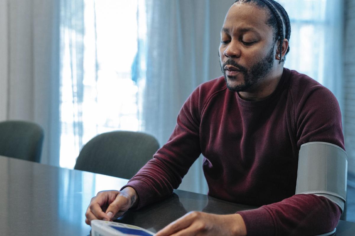 Man sits at kitchen counter and uses a blood pressure cuff