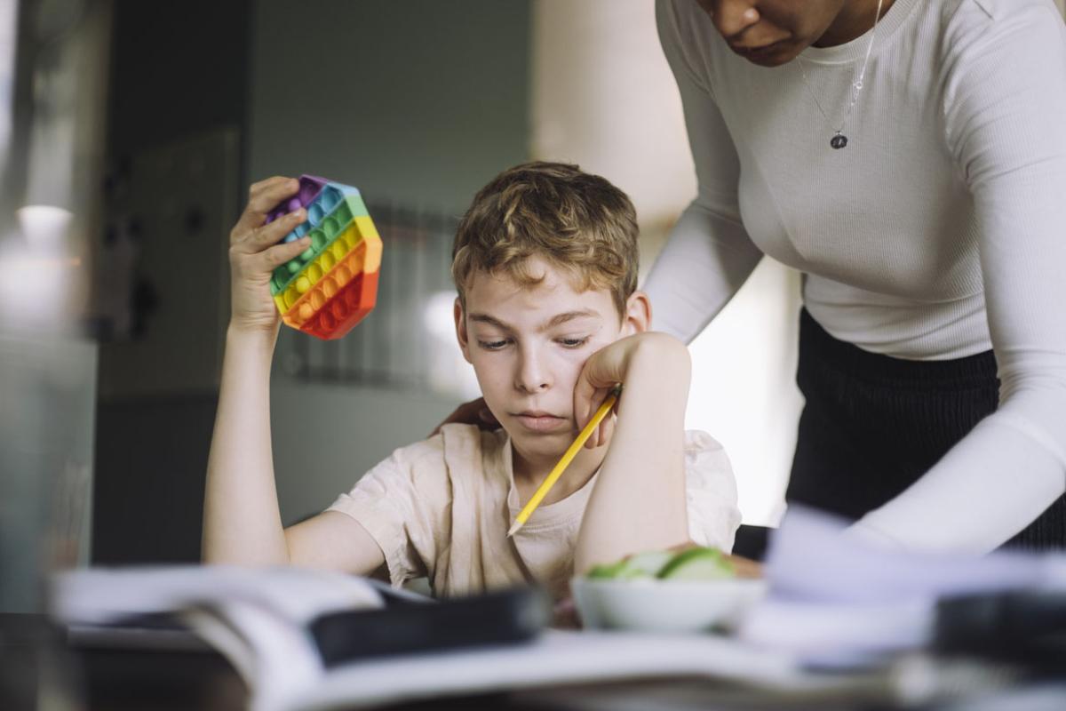 Parent assisting child holding push pop toy while doing studies at home