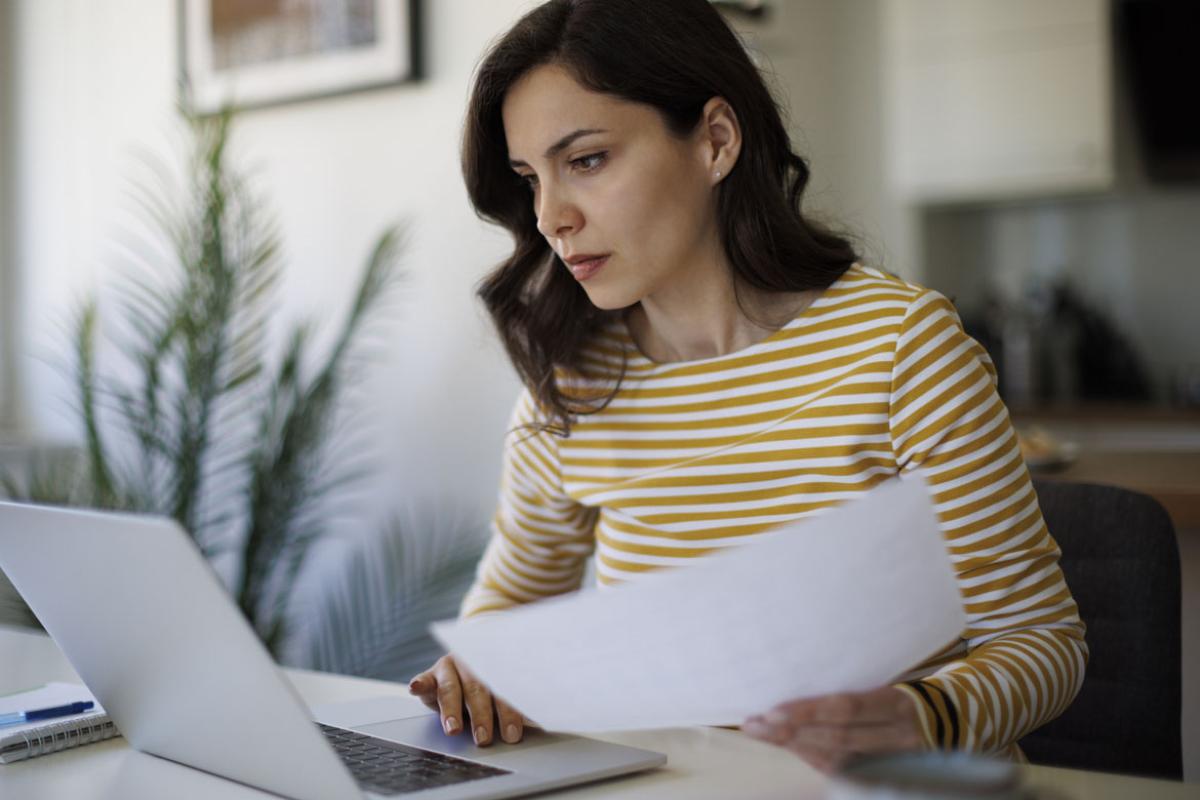 Young woman on laptop reviewing paperwork