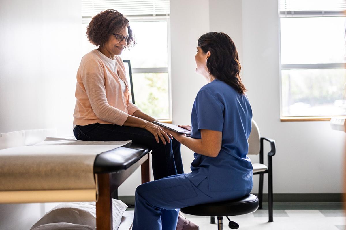 Smiling patient sits on an exam table while talking to health care worker