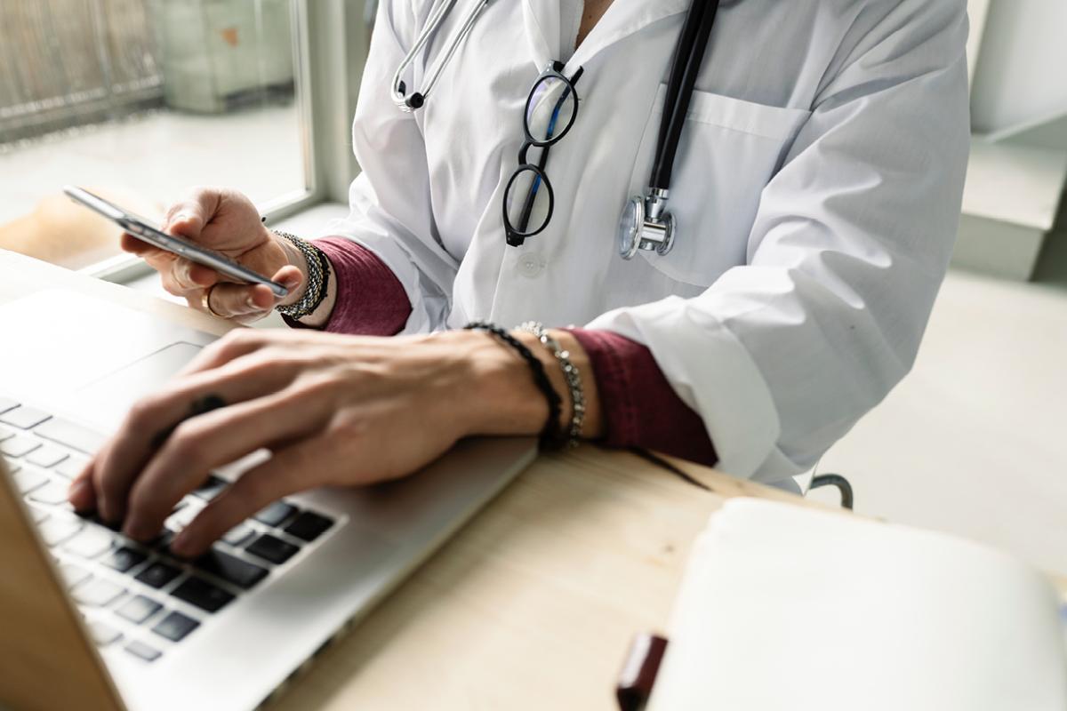 Doctor typing on laptop at desk with stethoscope around their neck